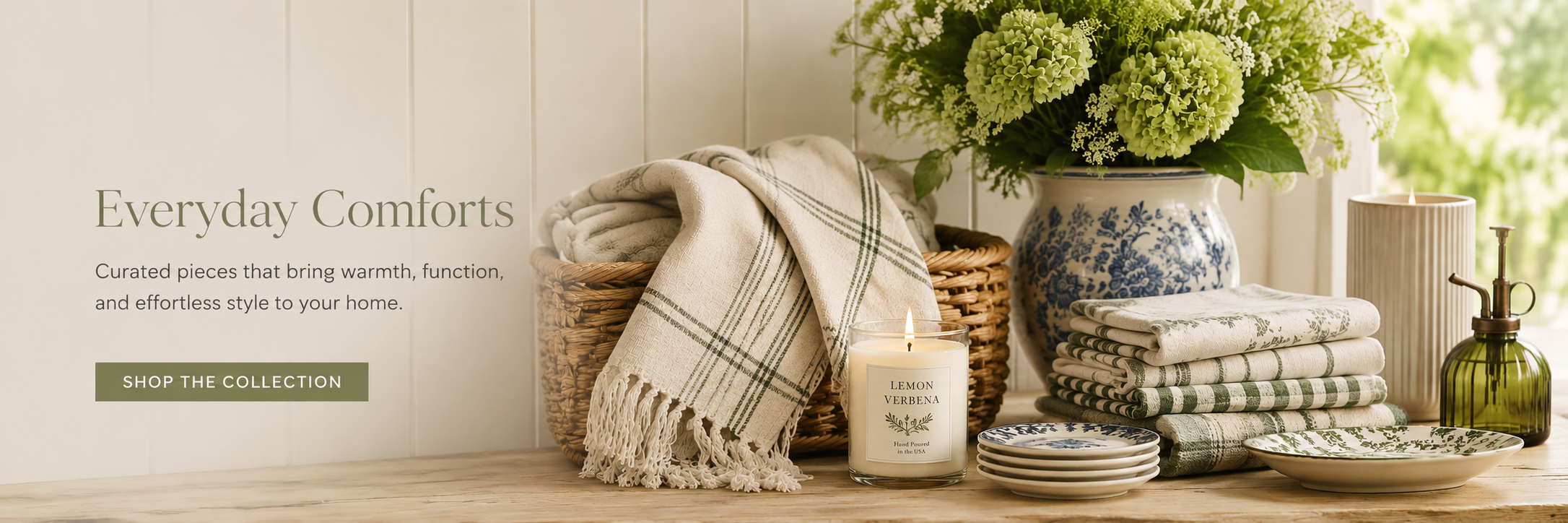 A curated collection of cozy home essentials including soft throws, kitchen linens, candles, entertaining pieces, and decorative accents styled in a warm and welcoming living space.