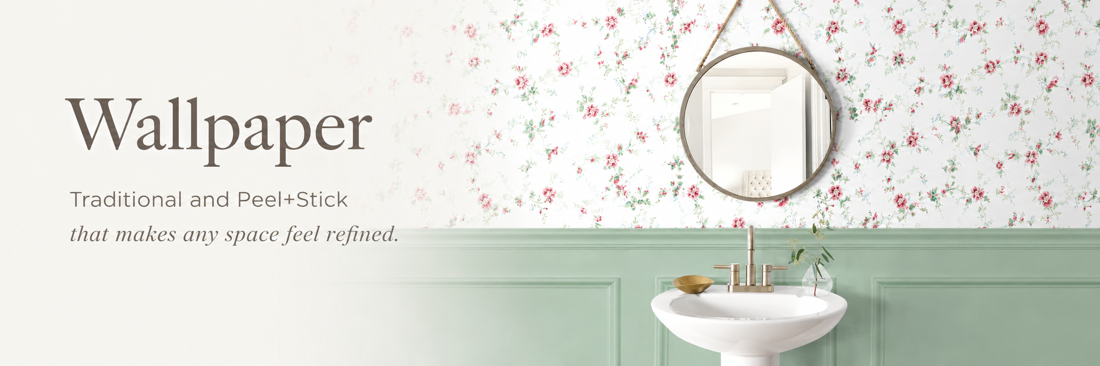 Wallpaper banner featuring pink floral peel and stick wallpaper, sage green wainscoting, a round mirror, and a white pedestal sink in a refined bathroom setting.