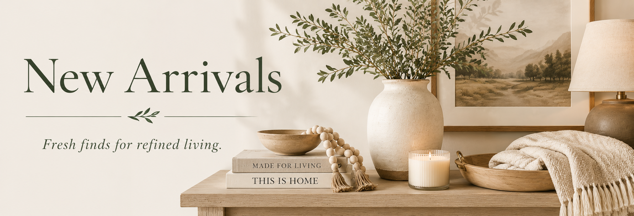 New Arrivals banner featuring a warm neutral home decor vignette with a ceramic vase, greenery, framed landscape art, candle, stacked books, wood bowl, lamp, and folded textured throw.