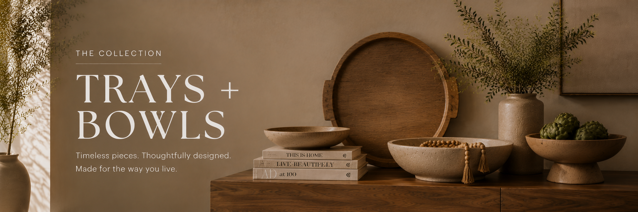 Neutral trays and bowls styled on a wood console with ceramics, books, and greenery in a warm, refined home setting